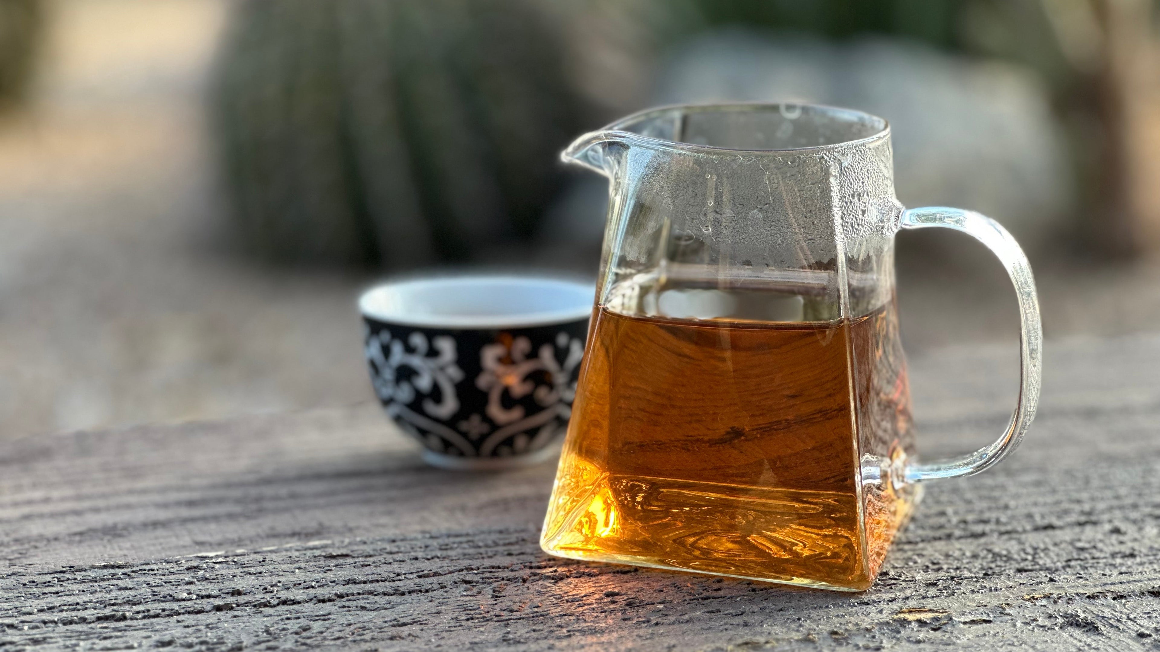 Clear glass pitcher with Desert Blossom tea on a wooden surface with blurred outdoor background
