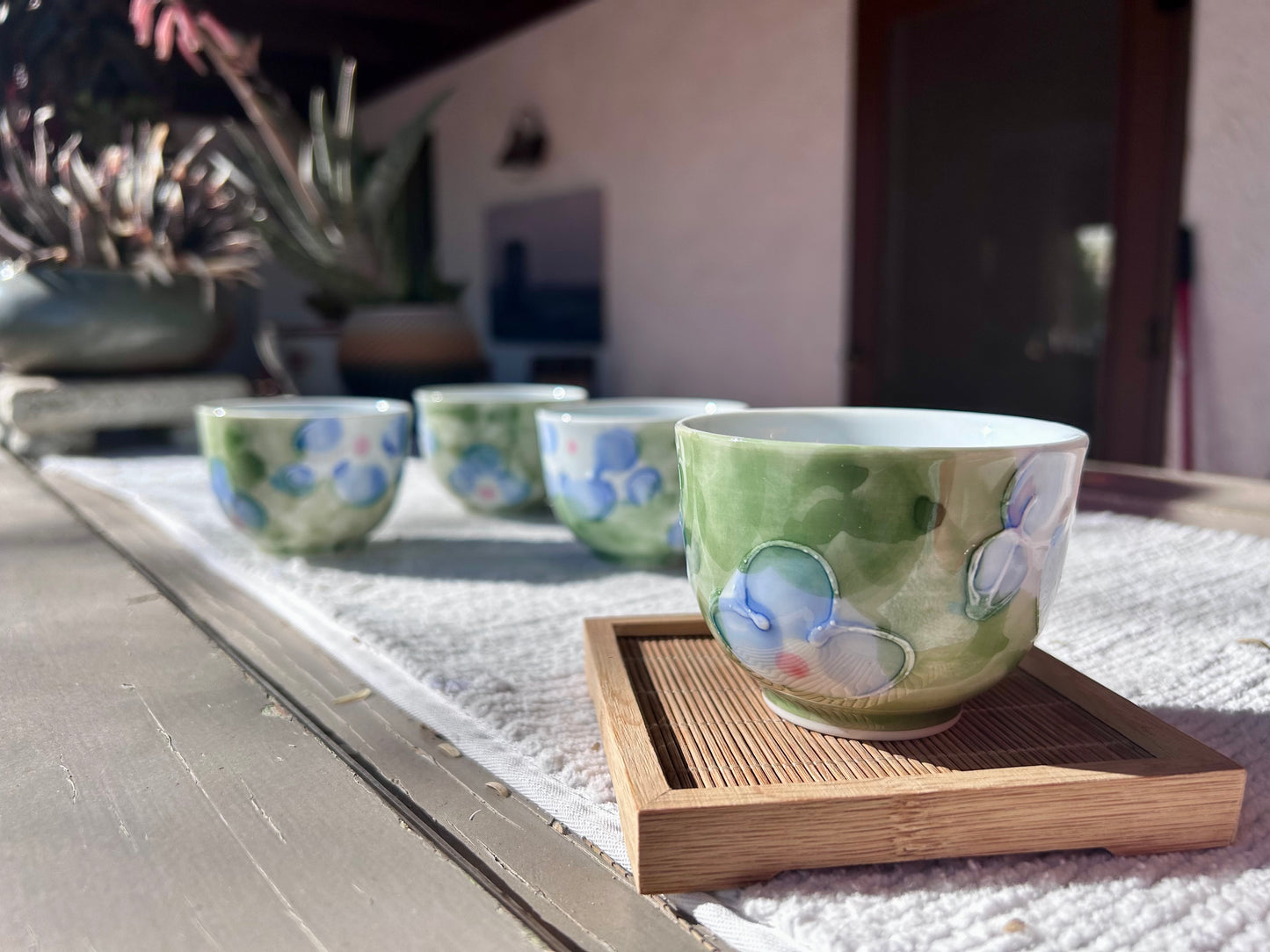 Set of ceramic cups with floral patterns on a wooden tray outdoors.