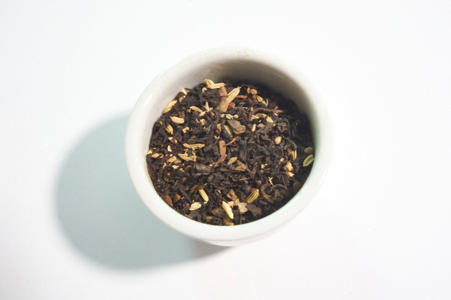 White bowl filled with dark brown tea leaves on a light gray background