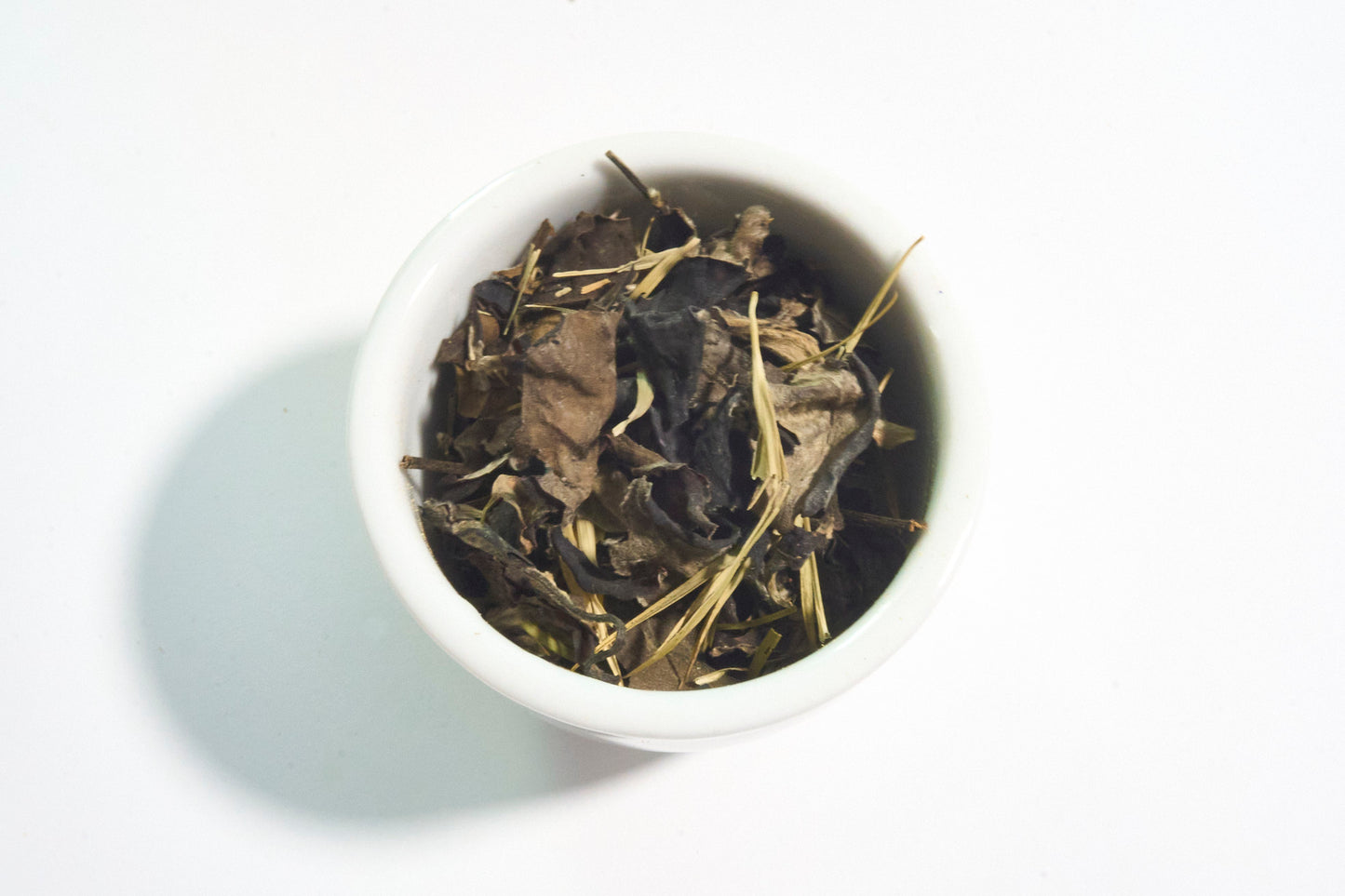 White bowl filled with dried tea leaves on a white background
