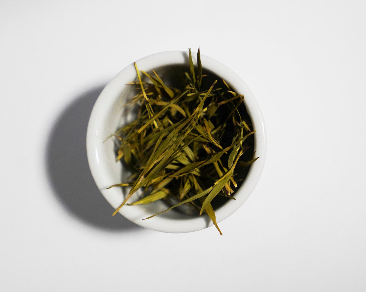 Bamboo tea leaves in a small white bowl on a light gray background