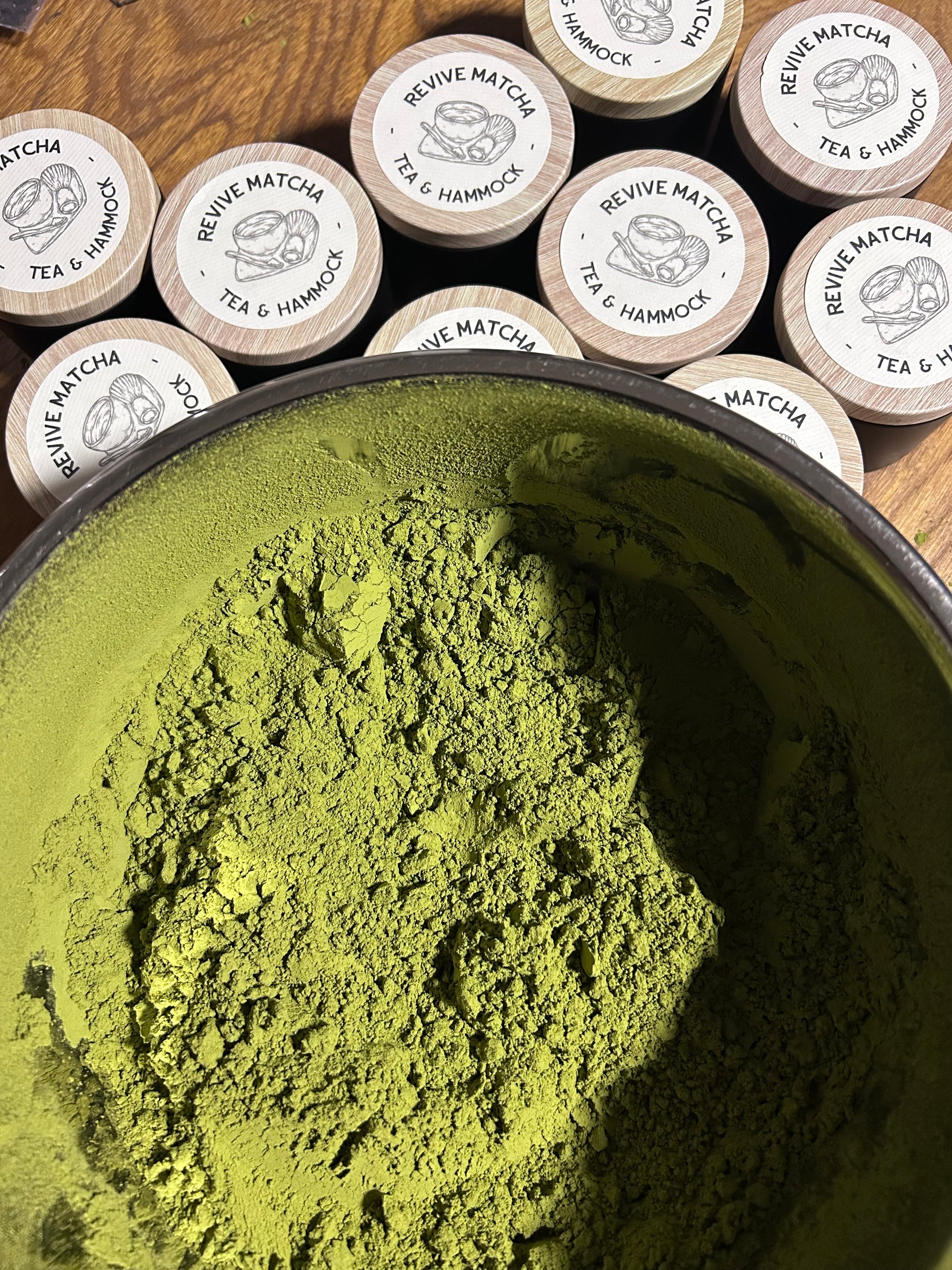 Matcha green tea powder in a black bowl with matcha containers on a wooden surface.