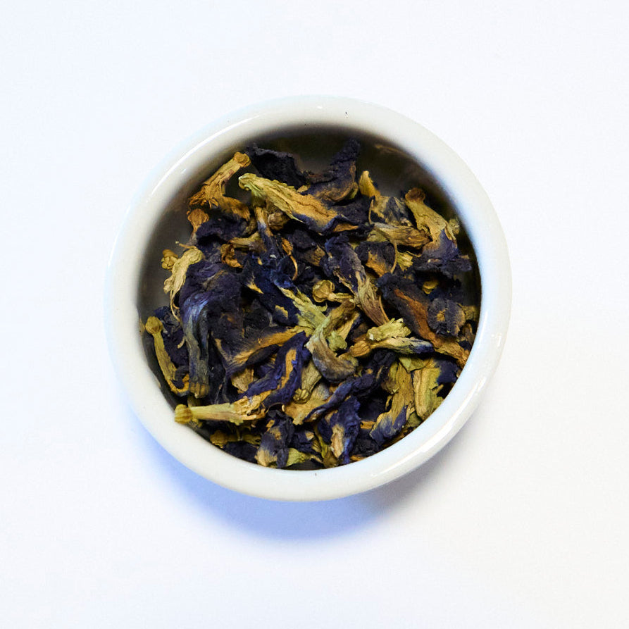 White bowl filled with dried blue and green tea leaves on a white background