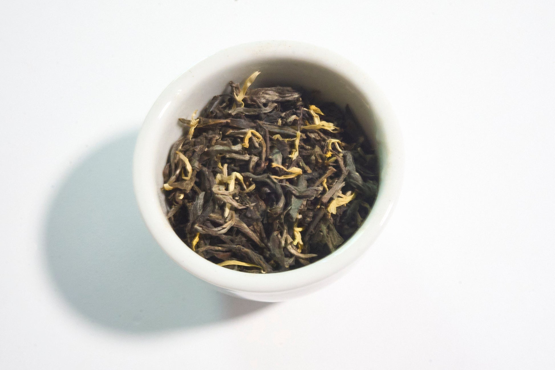 White bowl filled with black tea leaves on a white background