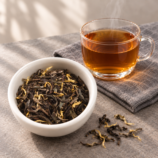 A white bowl filled with Earl Grey Puer loose-leaf tea and a clear glass cup of brewed amber tea on a gray cloth, with a few tea leaves scattered on a textured gray surface.