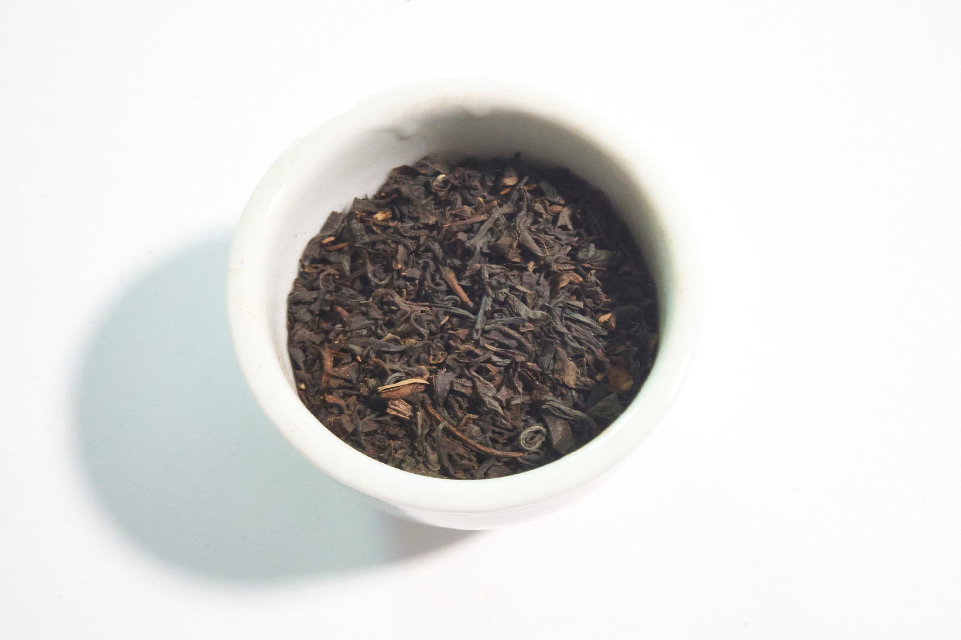 White bowl filled with dark brown tea leaves on a white background