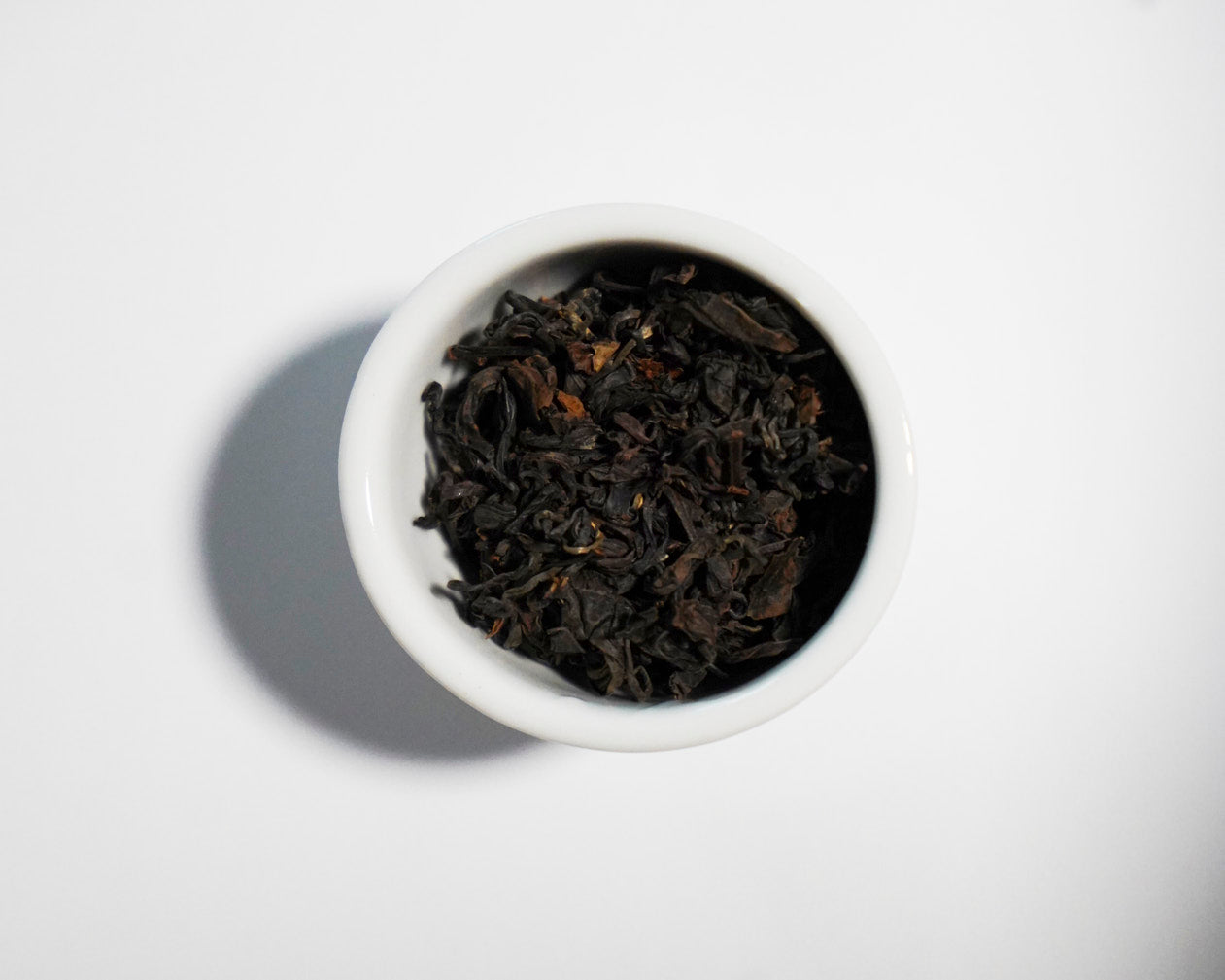 White bowl filled with GABA Oolong black tea leaves on a white background