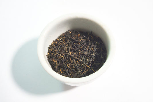 White bowl filled with black tea leaves on a white background
