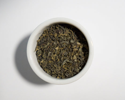 White bowl filled with green tea leaves on a white background