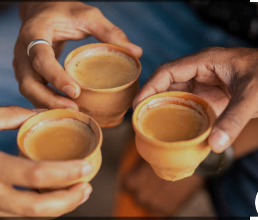 Three hands holding small terracotta cups filled with Travelers Chai by Tea & Hammock against a softly blurred background.