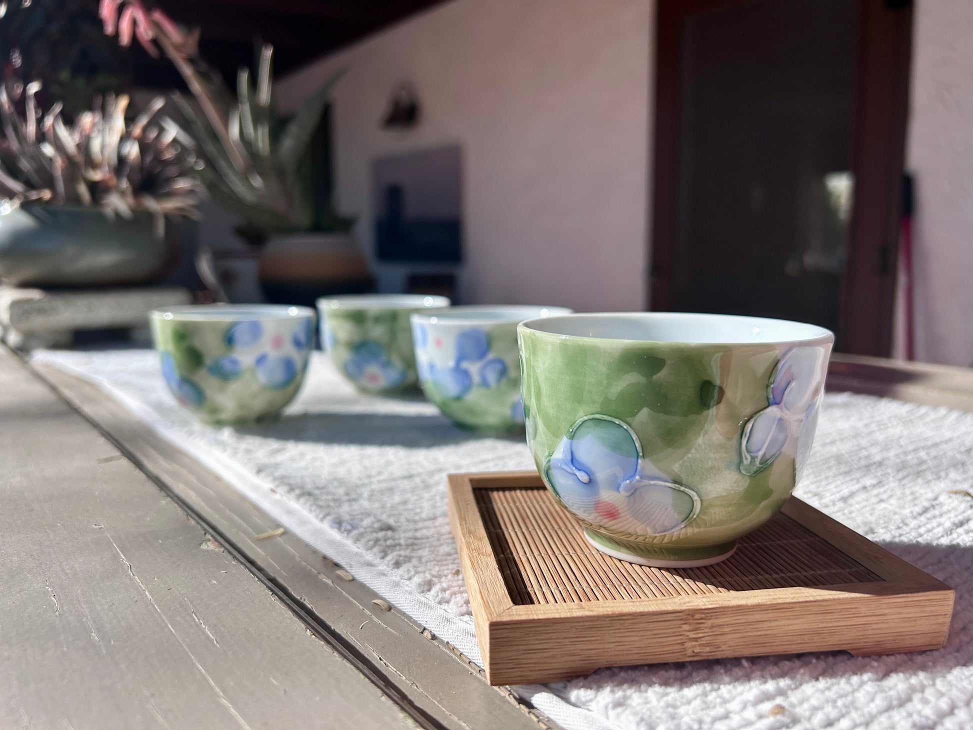 Set of ceramic cups with floral patterns on a wooden tray outdoors.