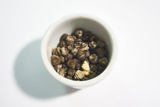 White bowl filled with dark green tea leaves on a white background