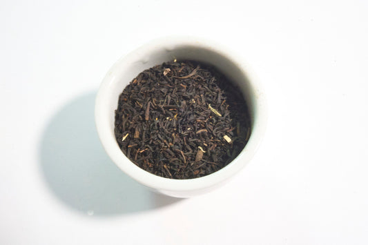 White bowl filled with black tea leaves on a white background