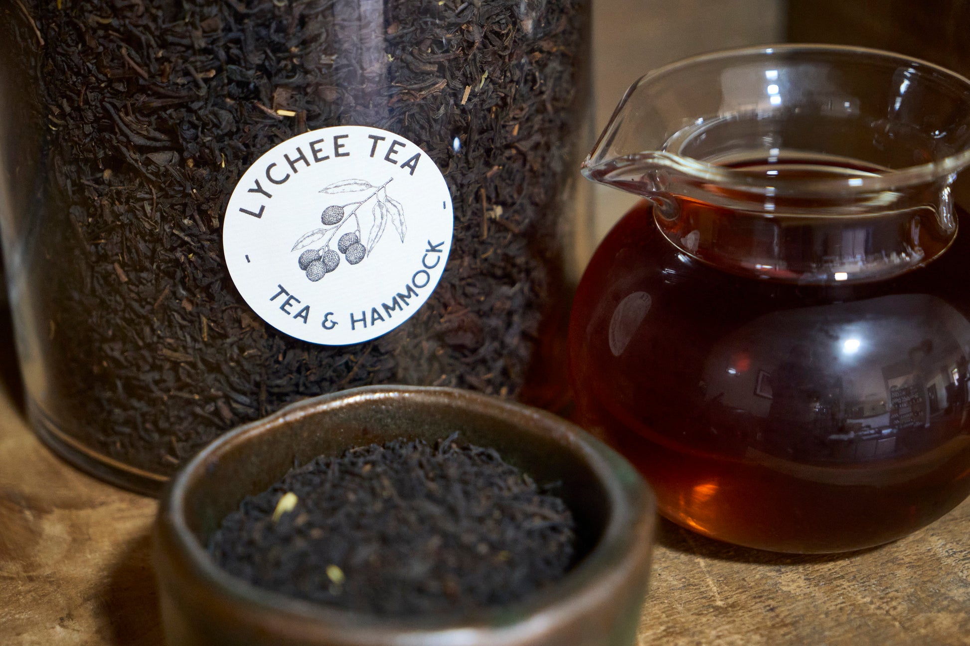 Lychee tea jar with a small bowl of tea leaves and a glass teacup on a wooden surface.
