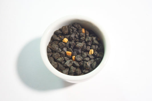 White bowl filled with dark green tea leaves on a light gray background
