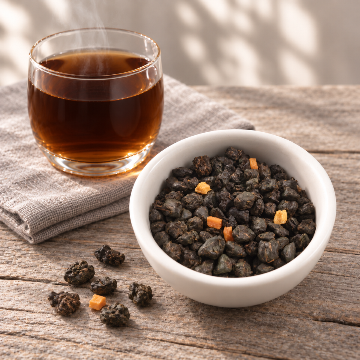 A white bowl filled with dark Mango Sticky Rice loose tea leaves and a glass of brewed amber tea on a rustic wooden table, with a folded linen napkin in the background.