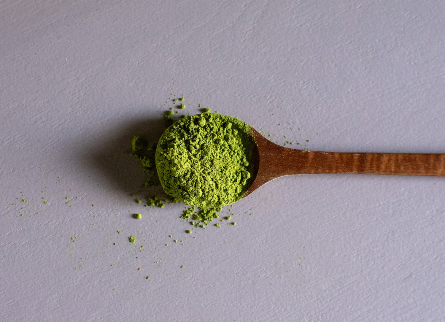 Wooden spoon with green powder on a gray background