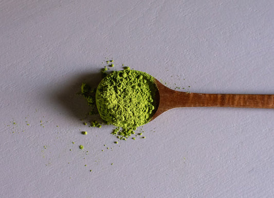 Wooden spoon with green powder on a gray background