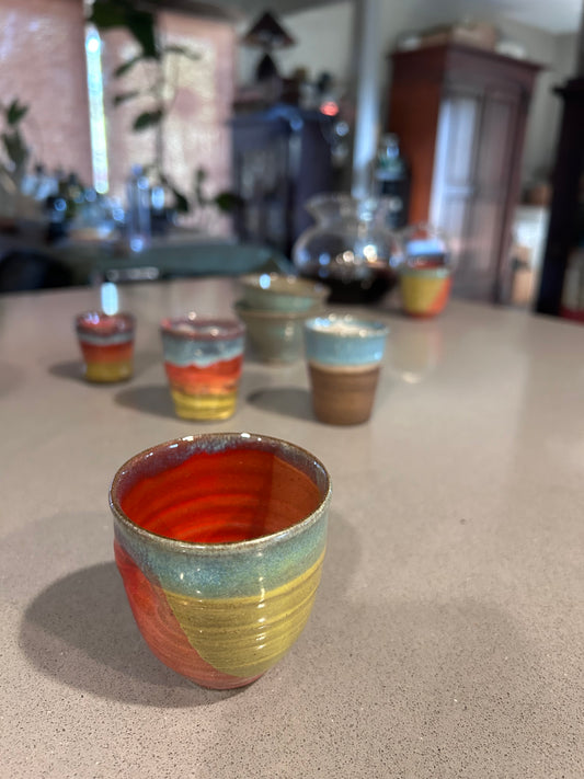 Colorful Scott Carlson ceramic tea cup on a textured surface with blurred background of other tea cups in the collection