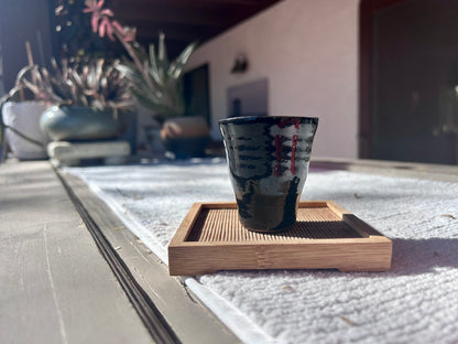 Ceramic cup with a wooden coaster on a reflective surface outdoors