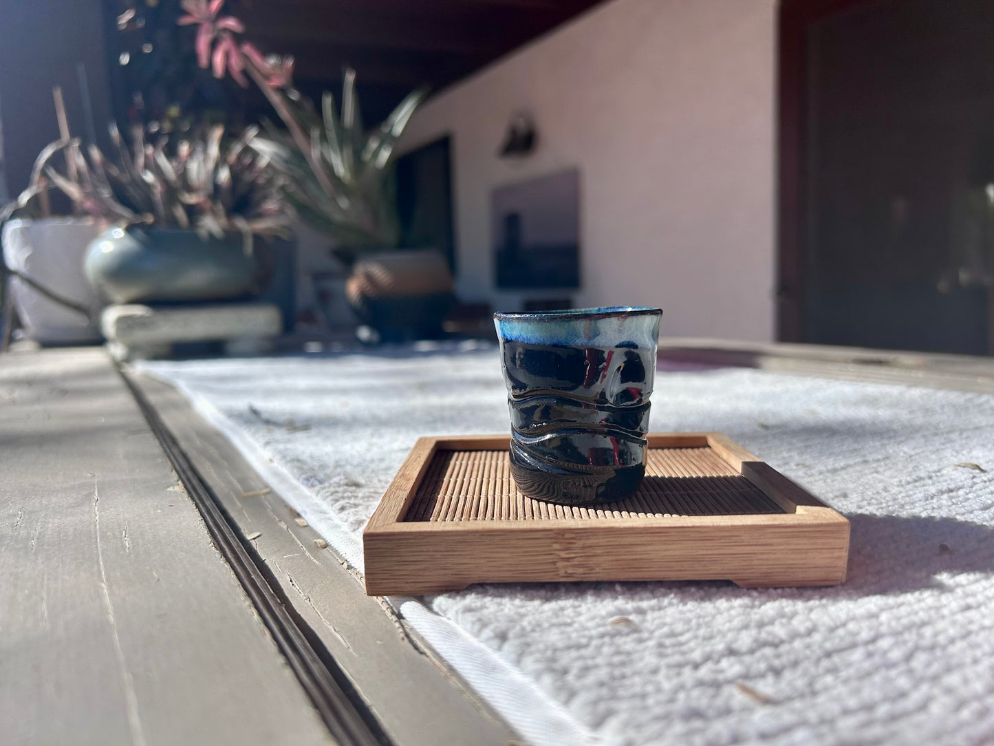 Blue glass cup on a wooden coaster with plants in the background
