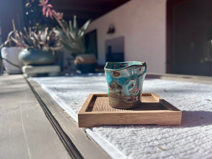 Decorative ceramic cup on a wooden coaster with plants in the background