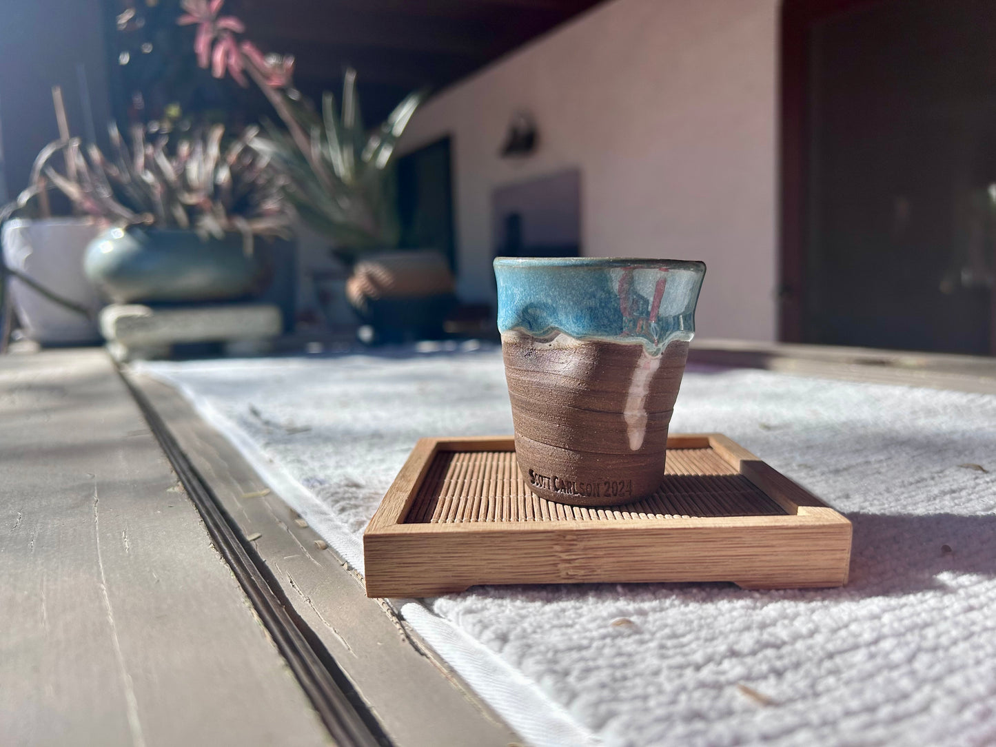 Ceramic cup with a wooden coaster on a reflective surface with plants in the background