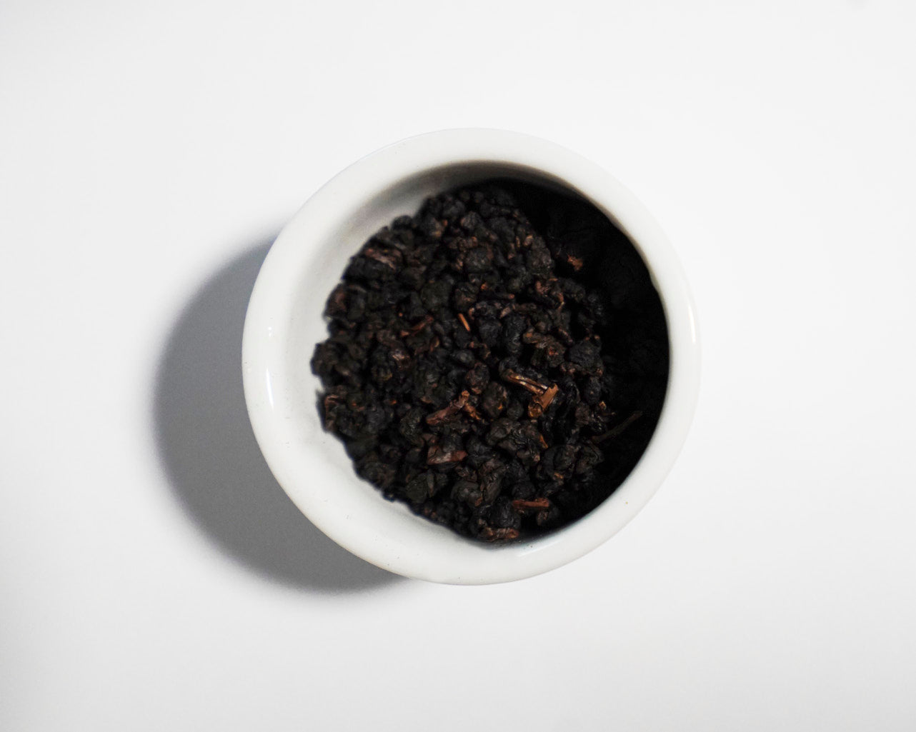 White bowl filled with dark brown Strong Fire tea leaves on a white background