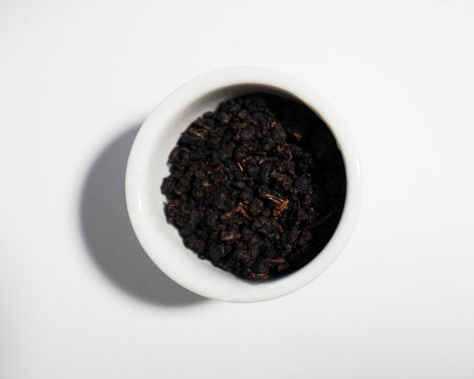 White bowl filled with dark brown Strong Fire tea leaves on a white background