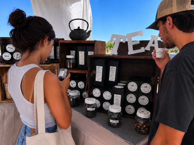 Two people at a tea stand with various tea products on display.