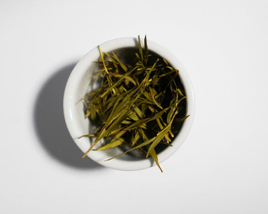 Bamboo tea leaves in a small white bowl on a light gray background