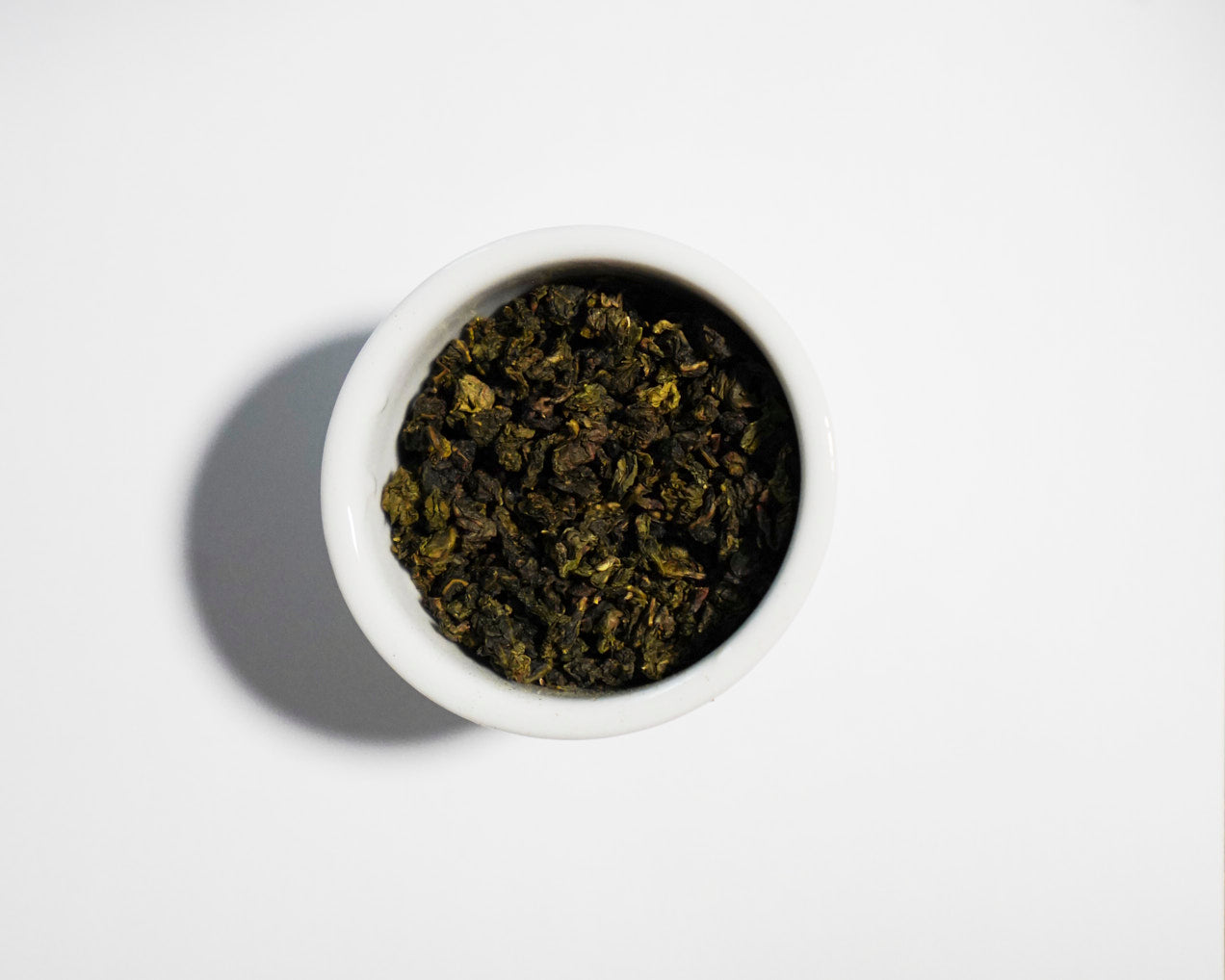White bowl filled with Zhu oolong green tea leaves on a white background