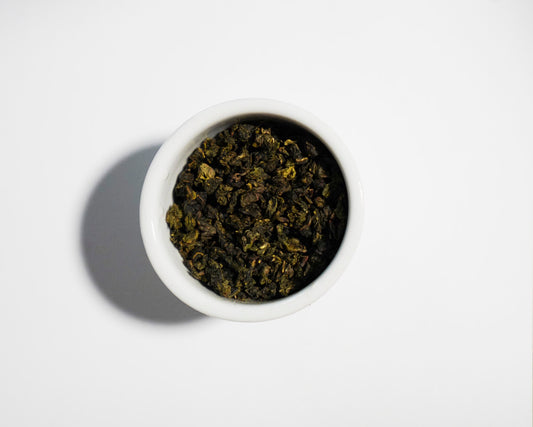 White bowl filled with Zhu oolong green tea leaves on a white background